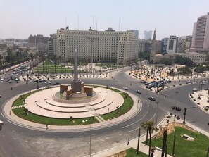 A roundabout with a central monument, surrounded by palm trees and a large building in the background. - Cairo Hub Hostel (Cairo)