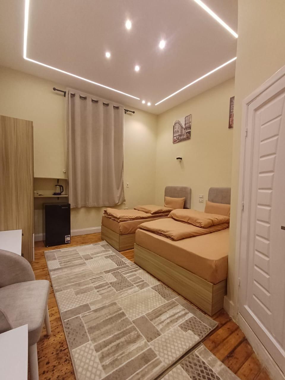 Ein Schlafzimmer mit zwei Betten, einem Schreibtisch, einem Stuhl, einem kleinen Kühlschrank und einem gemusterten Teppich.