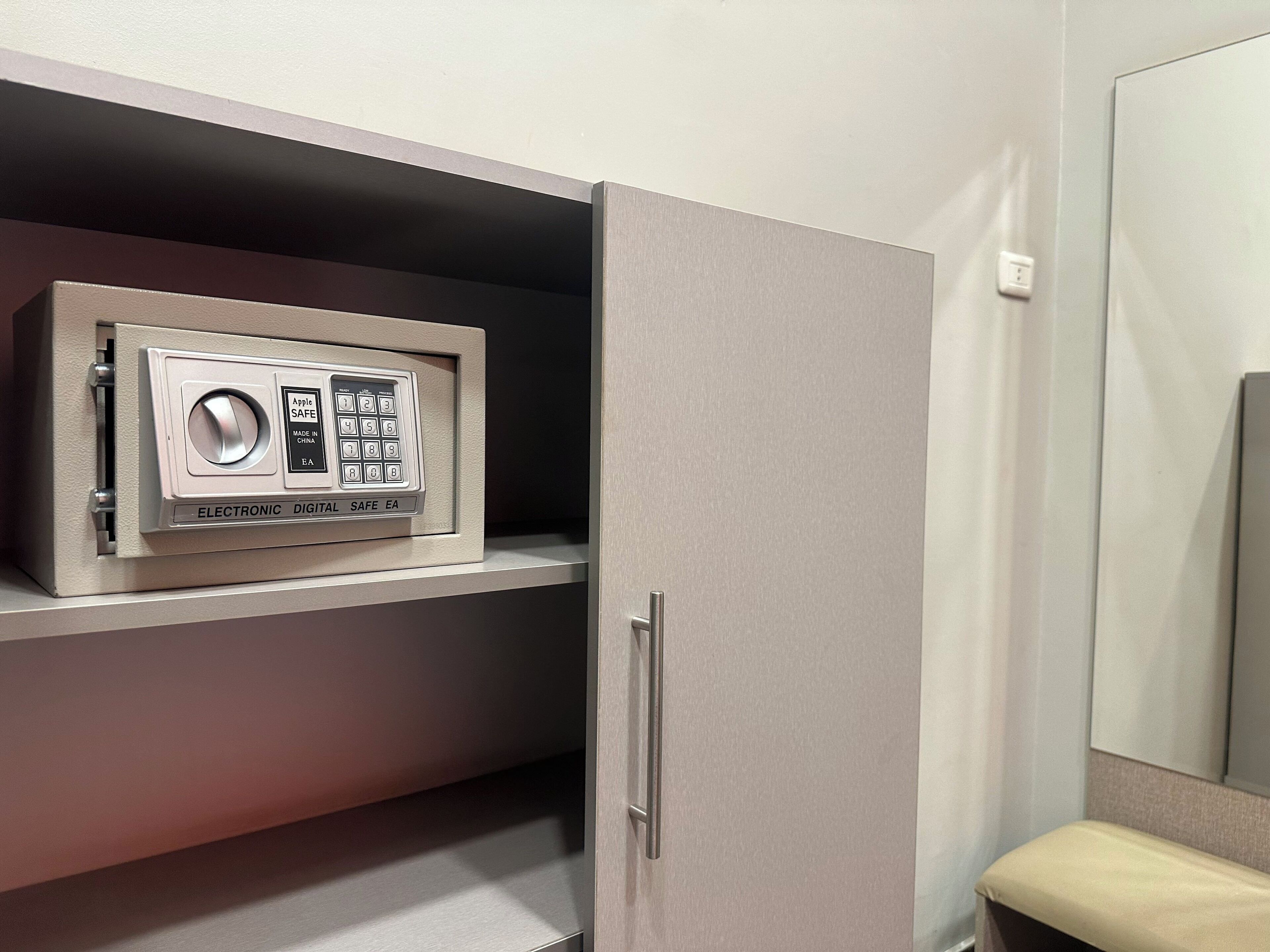 Een kluis met een keypad en een deurklink, geplaatst op een plank in een kamer met een spiegel en een bank.