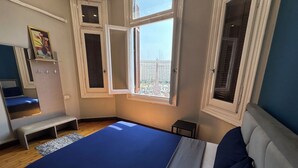 Una camera da letto con un letto, una panca, un tavolino e una finestra con vista sulla città.