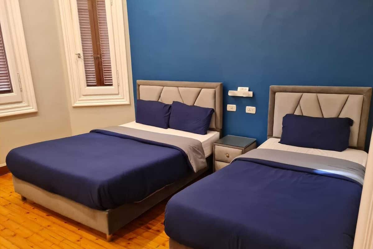 Ein Zimmer mit zwei Betten, jeweils mit Kopfstütze und Kissen, einem kleinen Nachttisch und einer Steckdose.