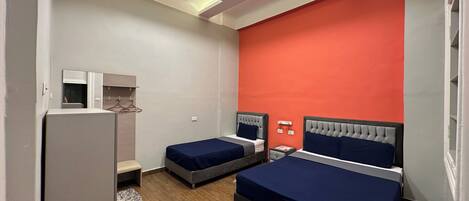 A hotel room with two beds, a wardrobe, a mirror, and a red accent wall.