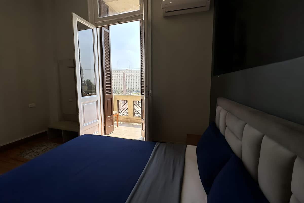 Ein Schlafzimmer mit Bett, Klimaanlage und einem Balkon mit Blick auf Gebäude.