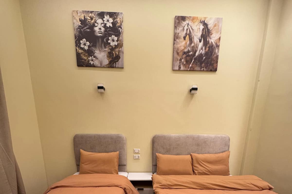 Ein Zimmer mit zwei Einzelbetten, Holzboden, einem gemusterten Teppich und zwei an der Wand befestigten Bildern.