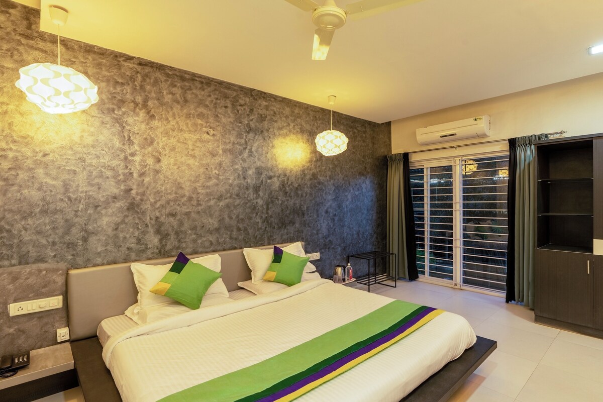 A modern bedroom with a large bed, a ceiling fan, an air conditioning unit, and a view through the window.
