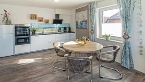 Een moderne keuken met witte kasten, een ingebouwde oven en een eetgedeelte met een ronde houten tafel en metalen stoelen.