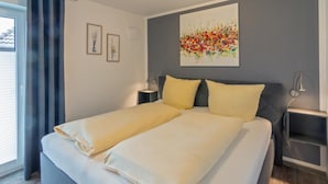 Cama doble con sábanas blancas, cabecera gris y dos mesitas de noche con lámparas.