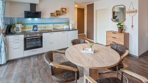 Una cocina moderna con armarios blancos, horno empotrado y una mesa de madera redonda con cuatro sillas.