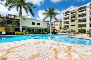 A hotel with a swimming pool, palm trees, and a multi-story building with balconies.