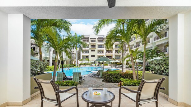 A balcony with two chairs and a table, overlooking a swimming pool and a building with balconies. - Condo 1 one bed, Palm Beach (Noord)