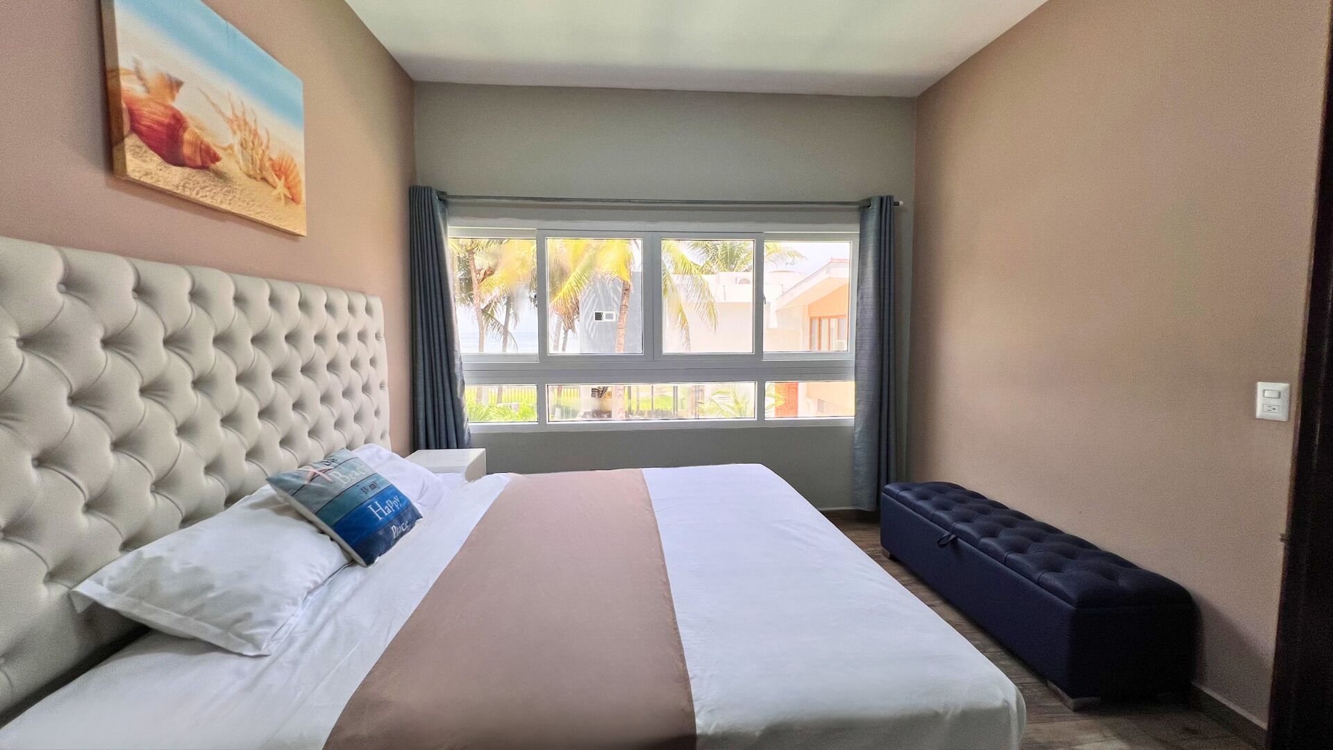 Een hotelkamer met een groot bed, een hoofdeinde, een raam met gordijnen en een schilderij aan de muur.