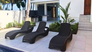 A poolside area with three lounge chairs, a modern building with a large window, and a wooden door. - Sofy House (La Libertad)
