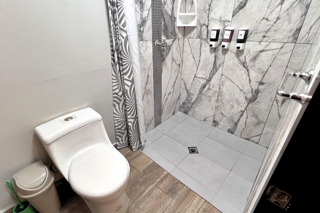 A bathroom with a toilet, a shower with a marble wall, and a tiled floor.