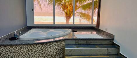 Ein Badezimmer mit einer großen Badewanne, einer Wand mit Fliesenmosaik und Meerblick durch ein großes Fenster.