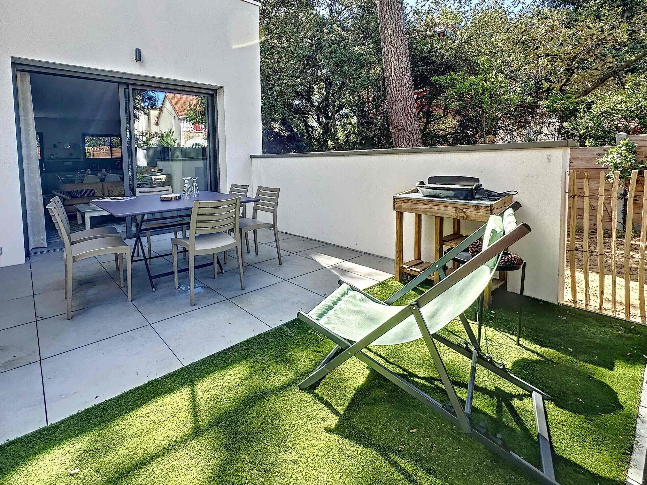 Eine Terrasse mit Tisch und Stühlen, ein grüner Rasen und ein Holzzaun.