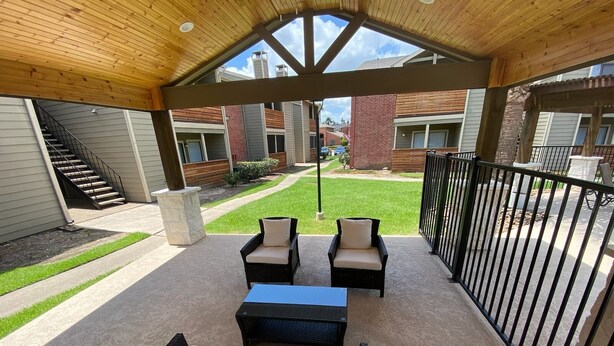 An outdoor patio with wicker furniture, a table, and a view of neighboring buildings. - Cozy 1BR Apt in Medical Center. Close to Downtown/ Zoo/ Medical Center  (Houston)