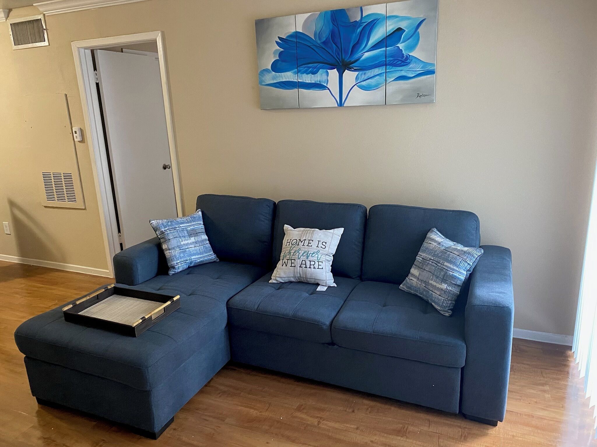 A living room with a dark blue sectional sofa, two matching throw pillows, a small side table, and a wall-mounted painting of a blue flower.