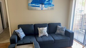 A living room with a dark blue sofa, a tray, and a wall-mounted painting. - Cozy 1BR Apt in Medical Center. Close to Downtown/ Zoo/ Medical Center  (Houston)