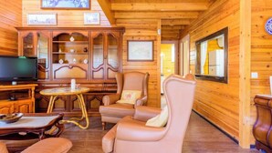 L’intérieur d’un chalet confortable, avec des murs en rondins, une télévision, des fauteuils en cuir, un meuble en bois et des tableaux encadrés.