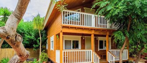 Una casa in legno a due piani con un balcone, immersa nel verde e decorata con piante in vaso.
