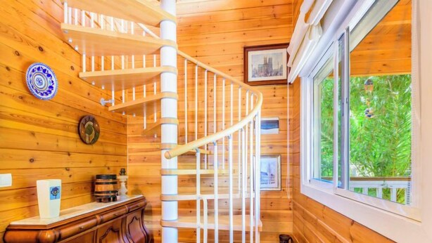 Un intérieur en bois avec un escalier en colimaçon, des murs en bois et une fenêtre donnant sur un paysage verdoyant.