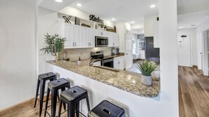 Una cocina moderna con armarios blancos, encimeras de granito y una isla central con taburetes de bar.