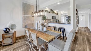 Una cocina moderna con armarios blancos, una mesa de comedor de madera y una lámpara colgante.