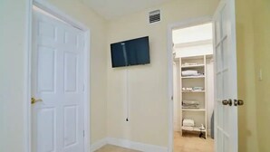 Ein Flur mit einer weißen Tür, einem an der Wand befestigten Fernseher und einem offenen Kleiderschrank mit Regalen.