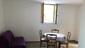 A room with a dining table and chairs, a purple sofa, and a window with a view of the outside. - Près du Parc de Verdure (Chomérac)