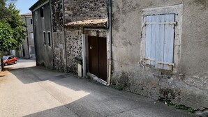 A narrow street with a stone building featuring a wooden door and a shuttered window. - Près du Parc de Verdure (Chomérac)