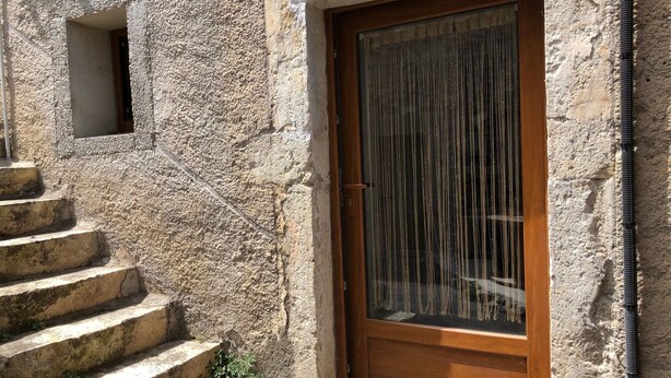 A stone building with a wooden door and a small window. - Près du Parc de Verdure (Chomérac)