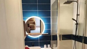Un baño con cabina de ducha de vidrio, un lavabo blanco con un espejo encima y una pared con azulejos azules.