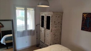 Un dormitorio con cama, armario, espejo y ventana.