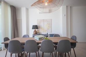Una sala da pranzo moderna con un tavolo in legno, sei sedie grigie, un vaso con fiori, un bicchiere da vino, una lampada e un quadro appeso al muro.