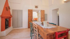 Un coin repas avec une table en bois, des chaises, une cheminée et une vue sur une autre pièce.