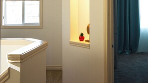 A room with a window, a small alcove with a plant, and a door leading to another room.