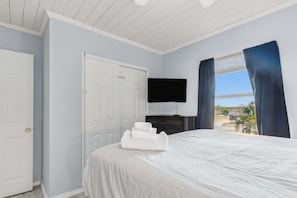 A hotel room with a bed, a flat-screen TV, a window with curtains, and a view of the outside.