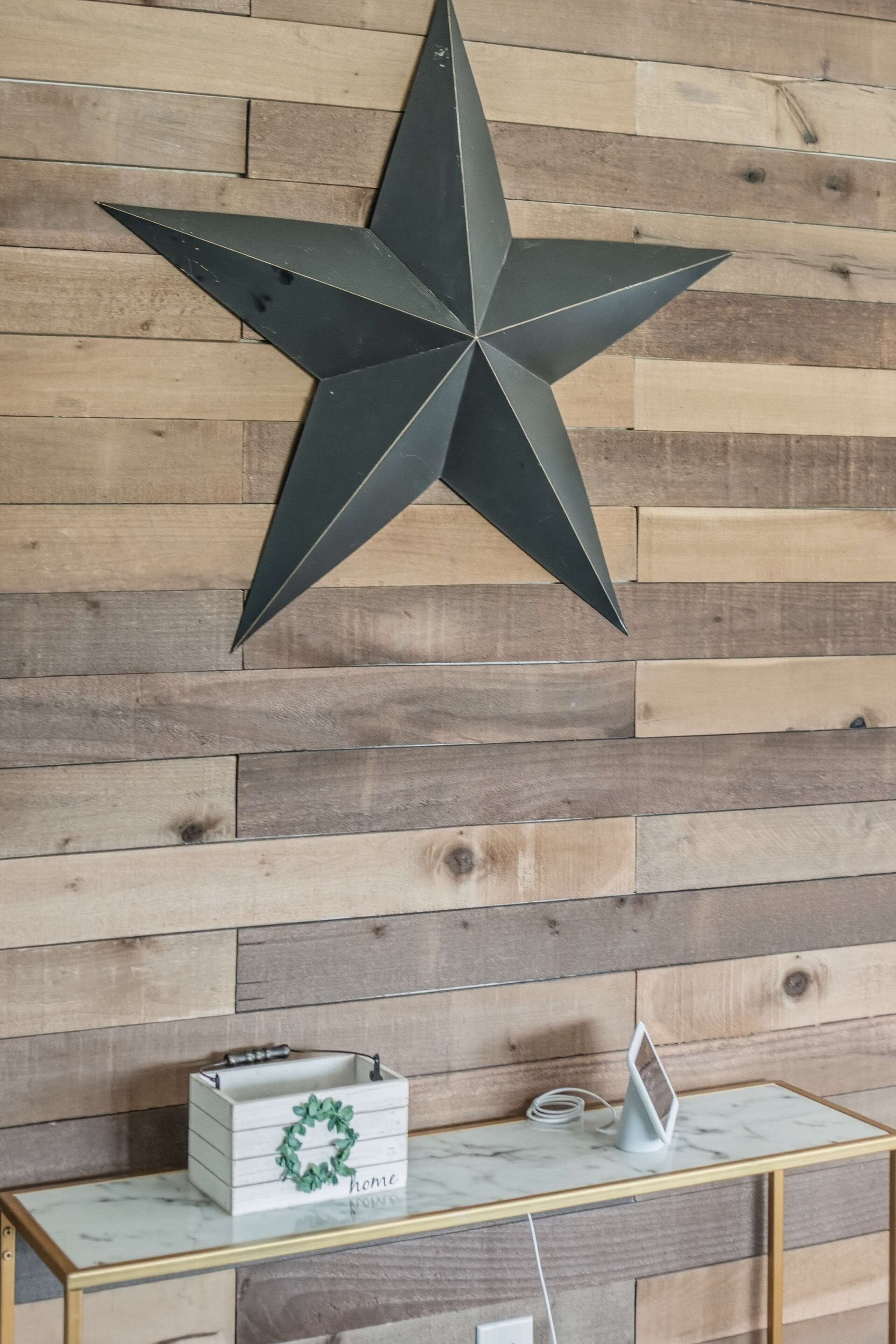 A star decoration on a wooden wall, a white box with a green wreath, and a small table with a white object on it.