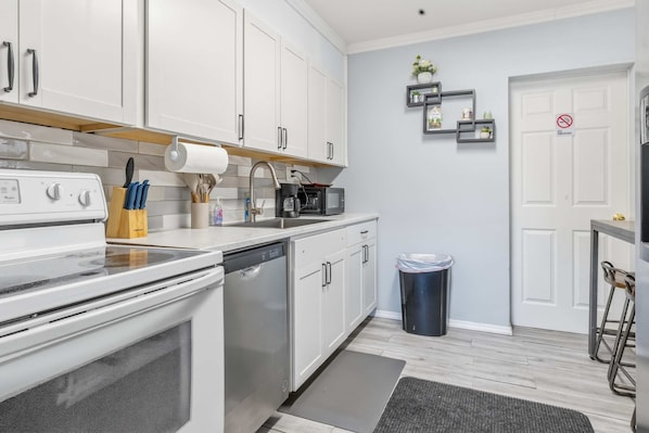 A modern kitchen with white cabinets, stainless steel appliances, and a black trash bin.