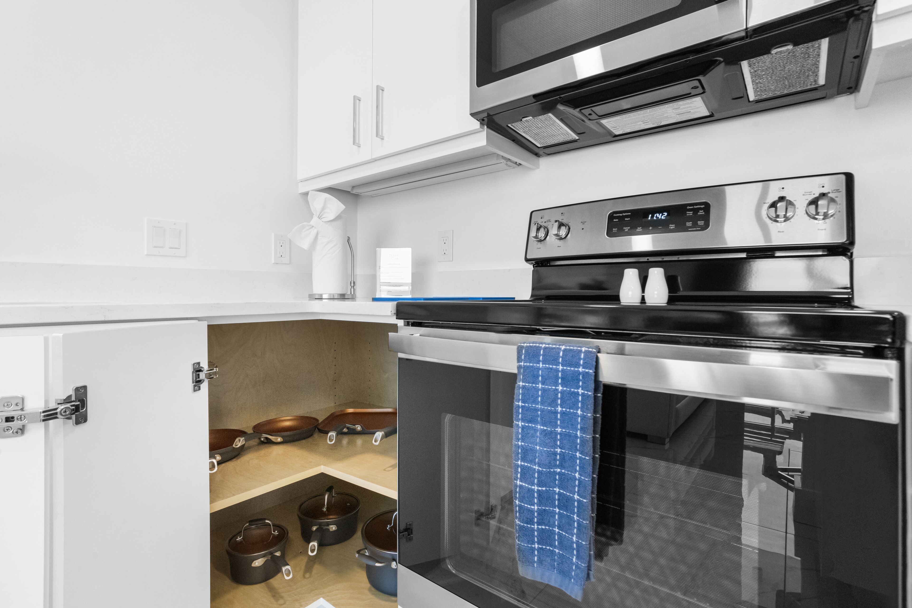 A kitchen with a built-in oven, a microwave above it, and a small window with a blue towel hanging.