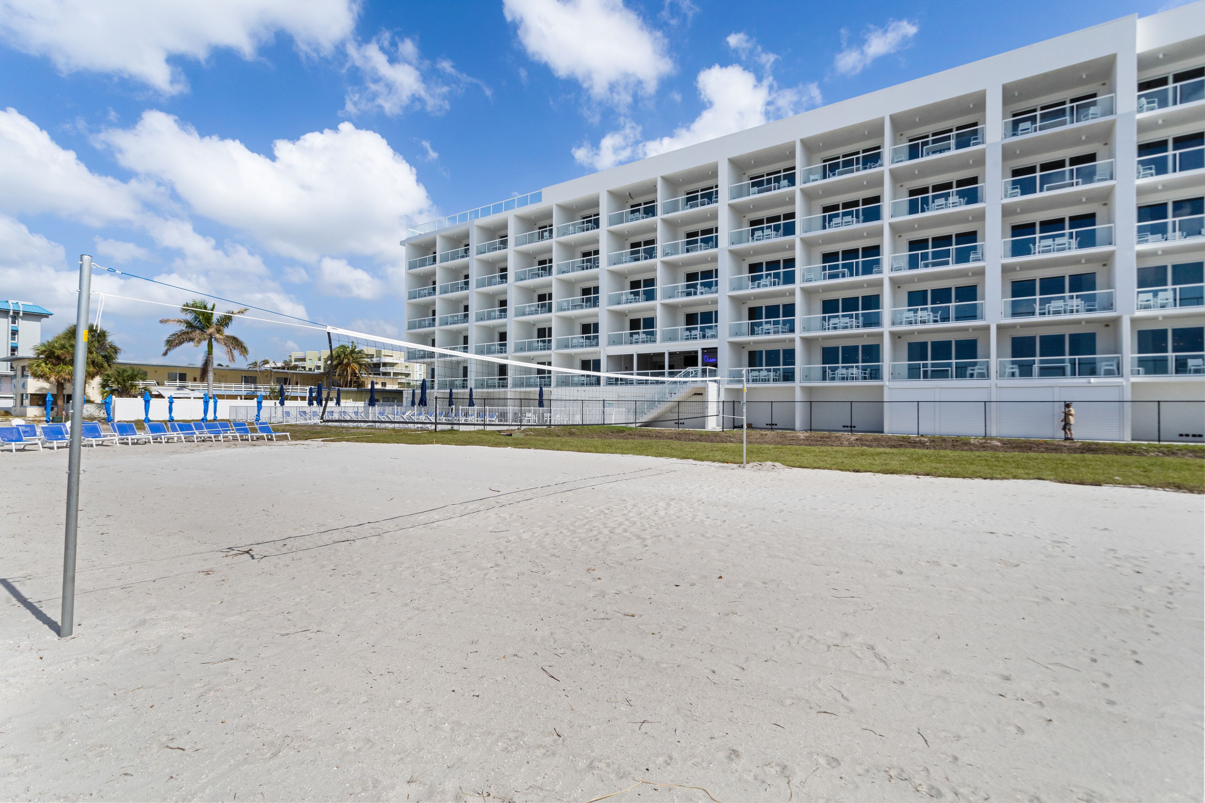 A modern hotel with multiple balconies, a sandy beach area, and a clear sky.