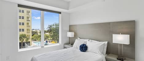 Ein modernes Hotelzimmer mit einem großen Bett, zwei Nachttischen, einem Deckenventilator und einem Fenster mit Blick auf Gebäude und Bäume.