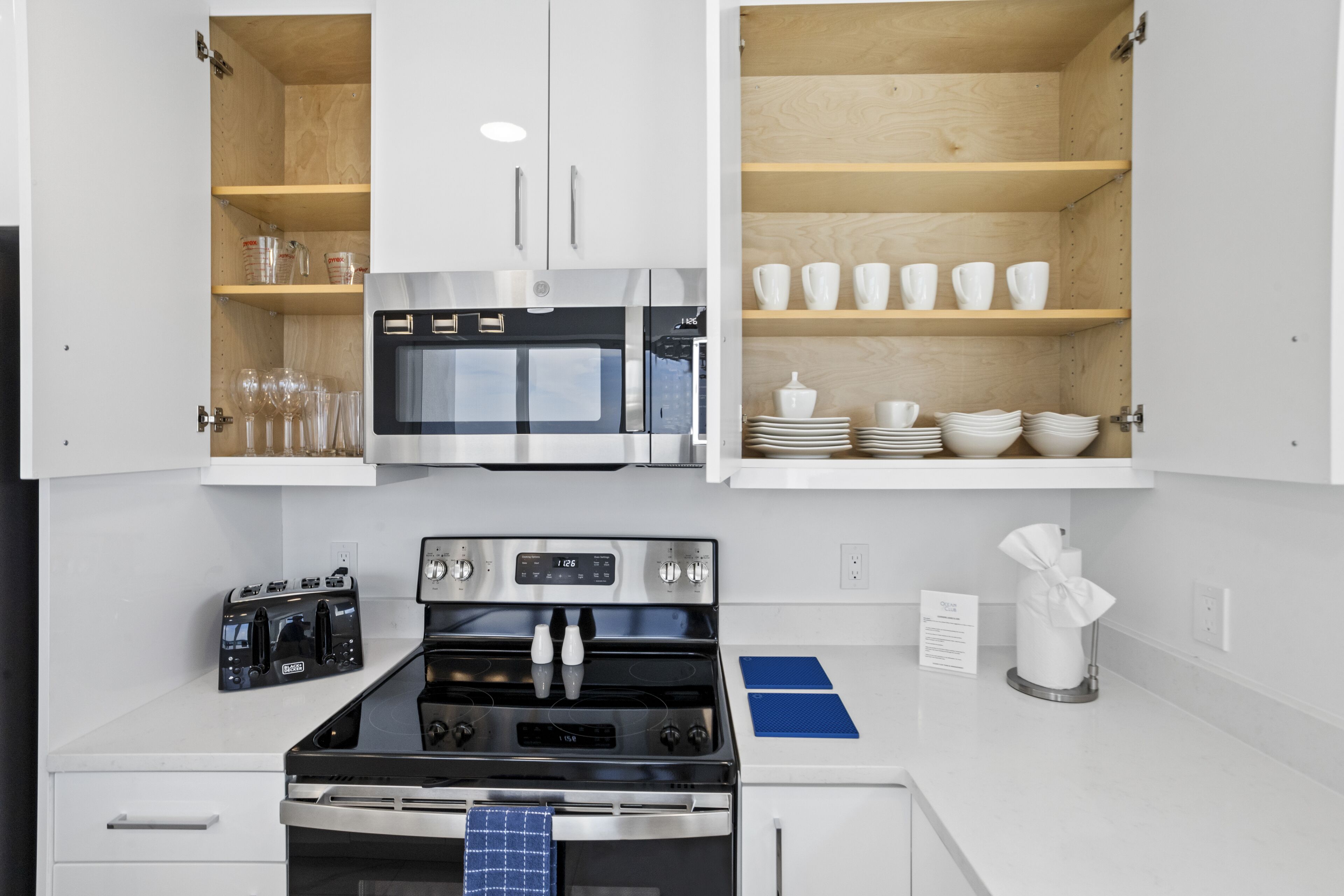 Une cuisine moderne dotée d’appareils électroménagers en acier inoxydable, d’étagères en bois et d’un aménagement épuré.