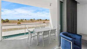 A balcony with a white table and chairs, a blue chair, and a view of the beach and ocean.