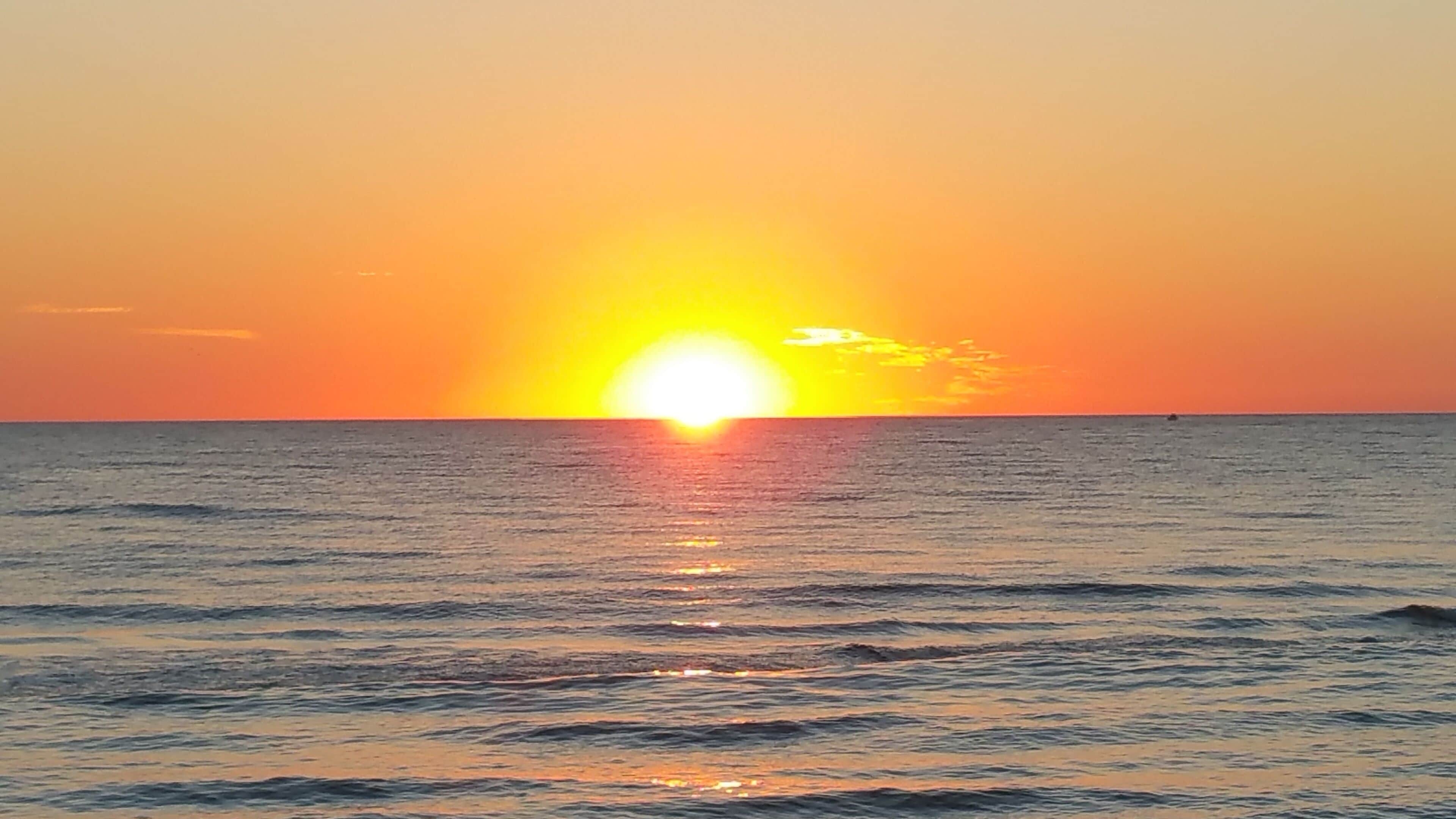 Un coucher de soleil sur l’océan, avec des eaux calmes qui reflètent le ciel.