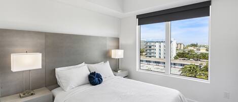 A modern hotel room with a large bed, two bedside tables with lamps, a ceiling fan, and a large window offering a city view.