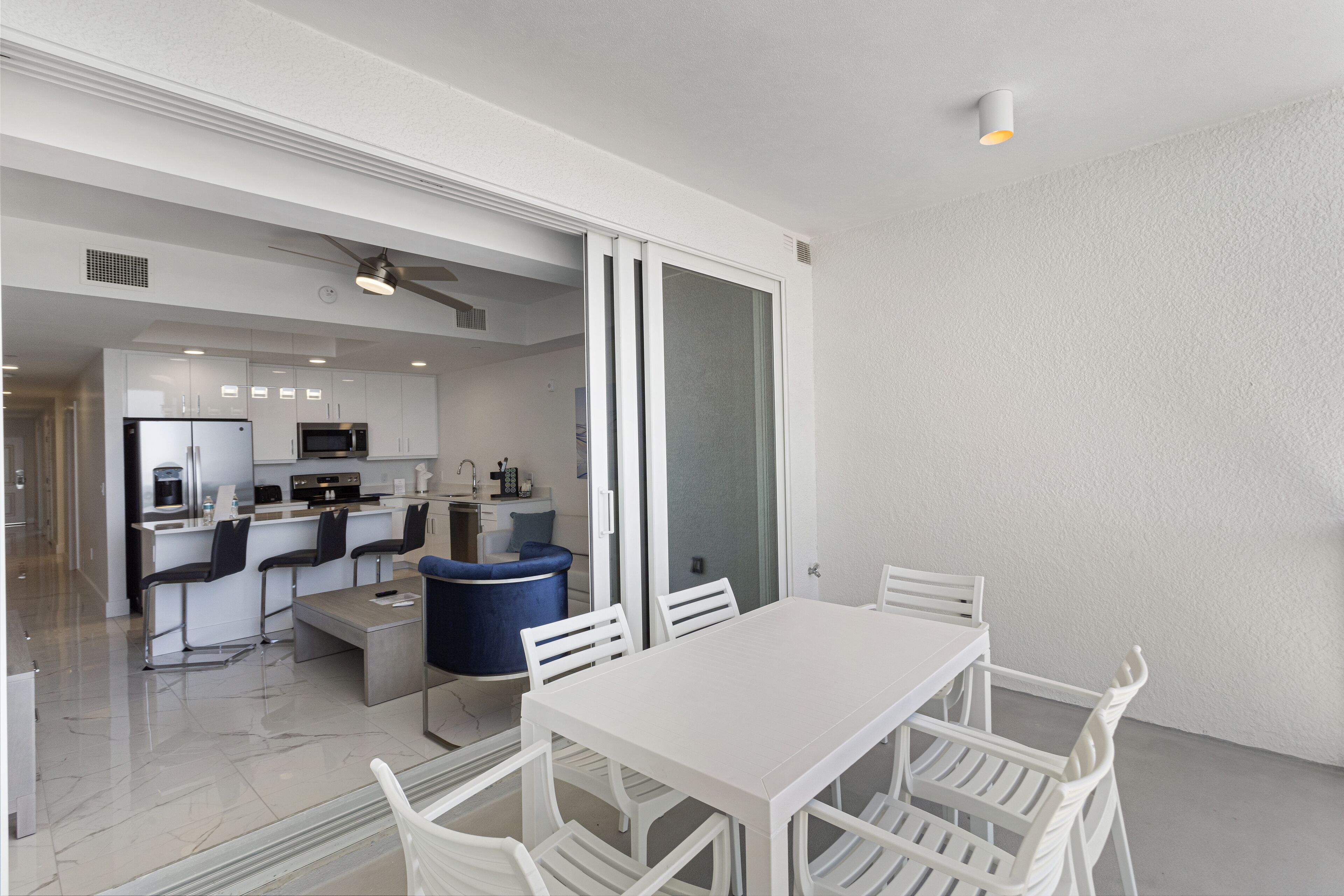 A modern kitchen with white cabinets, a refrigerator, and a microwave. There is a dining area with a white table and chairs.