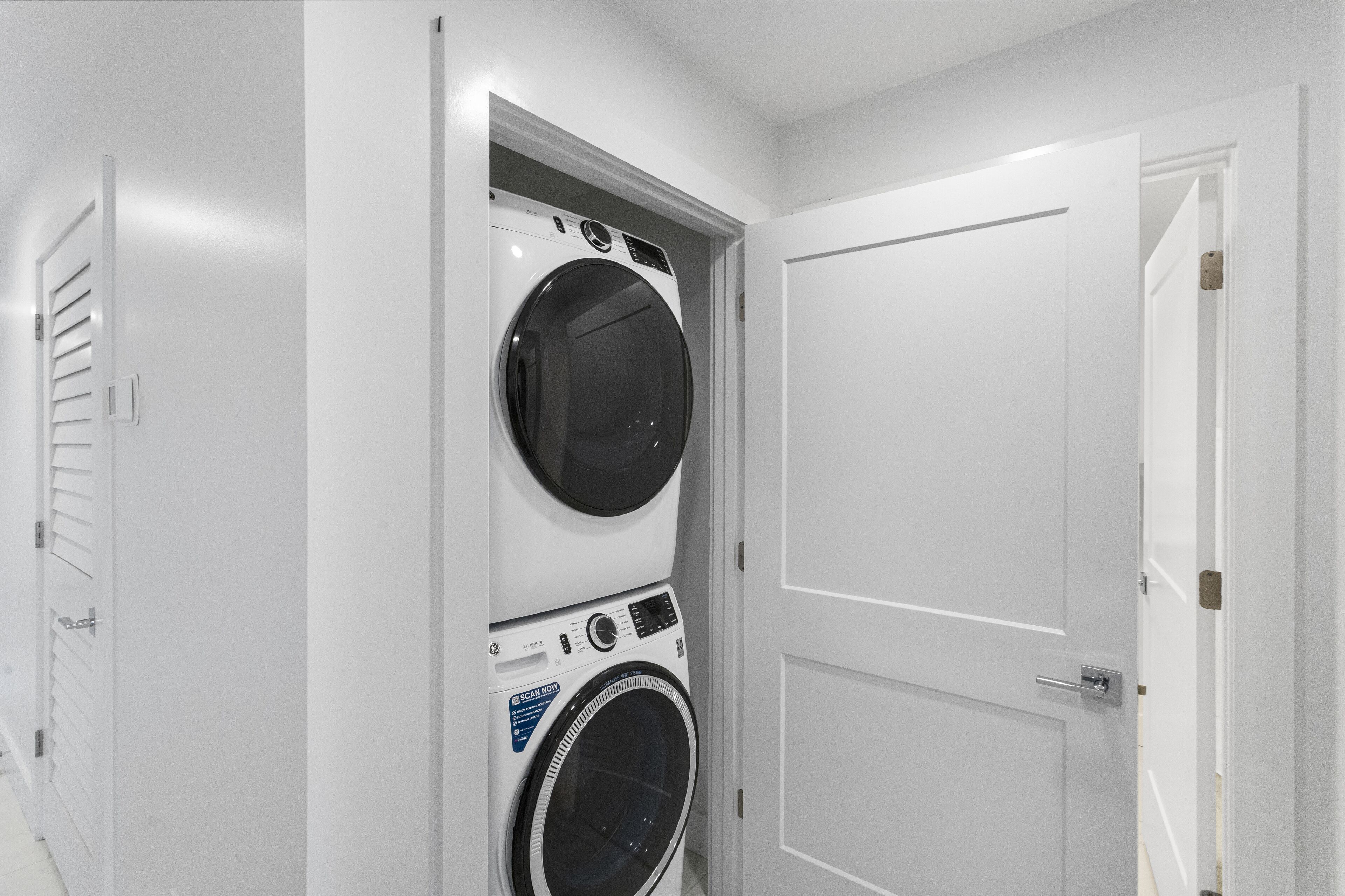 A laundry room with a front-loading washer and dryer, a door, and a vented wall.