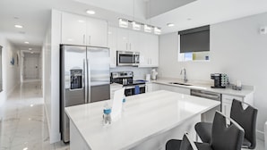A modern kitchen with white cabinetry, stainless steel appliances, and a central island with bar stools.