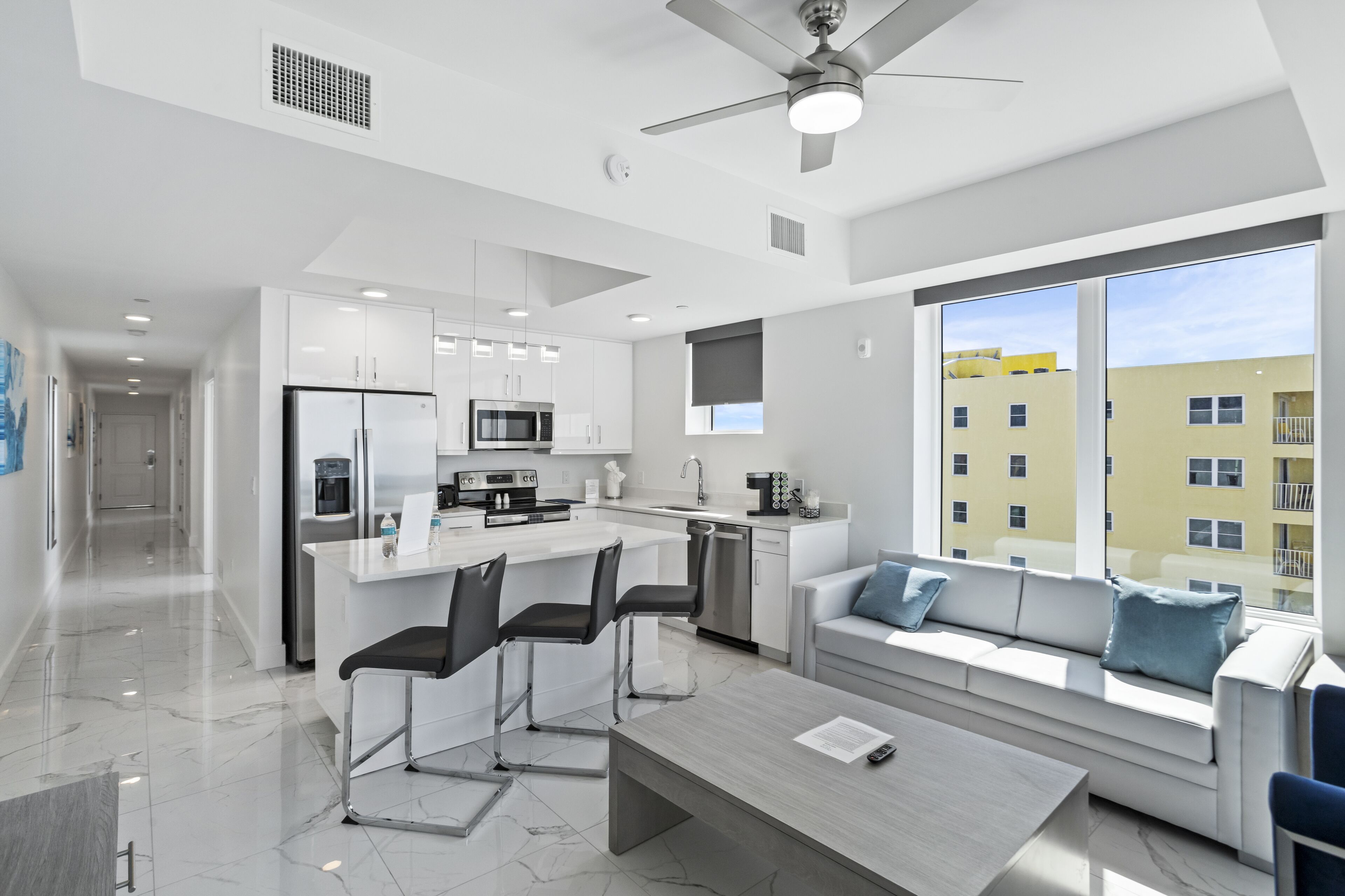 Una cocina moderna con armarios blancos, una isla central con taburetes y un comedor con mesa y sillas.